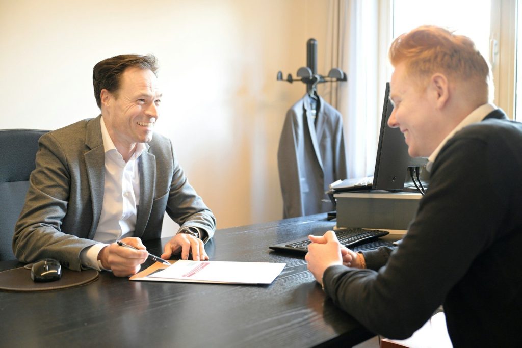 Two smiling men discussing documents at an office desk